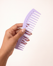 Hand holding the lavender wide-tooth detangling comb, showing its size and curved shape