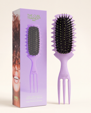 The Curl Trainer PRO curl defining brush in lavender with built-in volume pick, shown beside its box