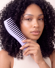 Woman with defined curls holding the lavender wide-tooth comb for curly hair beside her face